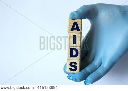 Aids Is An Acronym On Cubes Held By A Hand In A Blue Glove. Medical Concept.