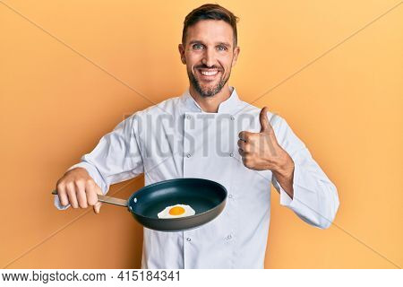 Handsome man with beard professional chef cooking fried egg smiling happy and positive, thumb up doing excellent and approval sign 