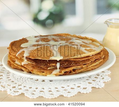 หวาน pancakes บนแผ่นกับนมข้นบนโต๊ะในห้องครัว