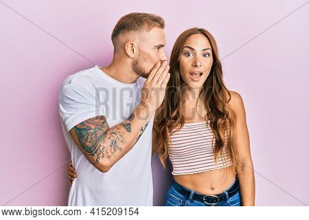 Young couple of girlfriend and boyfriend hugging and standing together hand on mouth telling secret rumor, whispering malicious talk conversation 