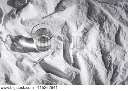 Glass Of Water On White Bedsheets Background. Drink Water Morning Routine. Stylish Fresh Mineral Sti