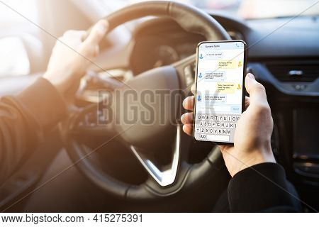 Man Typing Text Message On Mobile Phone While Driving Car