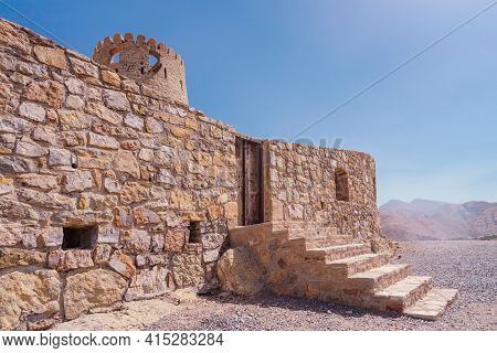 Stone Wall Of A Small Medieval Arabian Fort With Wooden Door And Stone Stairs In Bukha, Oman. Hazy D