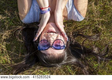 Happy Beautiful Young Woman In Sunglasses Smiles And Lies On A Meadow In The Grass In The Sunshine E