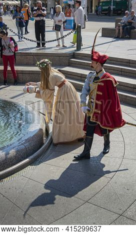 Zagreb, Croatia, September 2016 - Lady In Historic Costume Pouring Water Into A Fountain And A Sodie