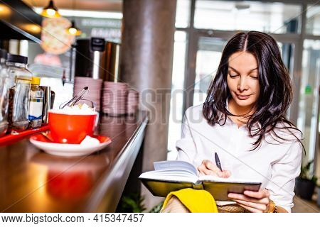 Indian Reading Notes In Notepad While Sitting Near Table Bar And Drinling Cup Of Tea