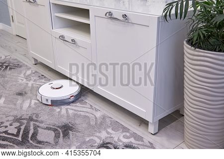 The White Robot Vacuum Cleaner Performs Automatic Cleaning Of The Gray Carpet. Smart Home Technology