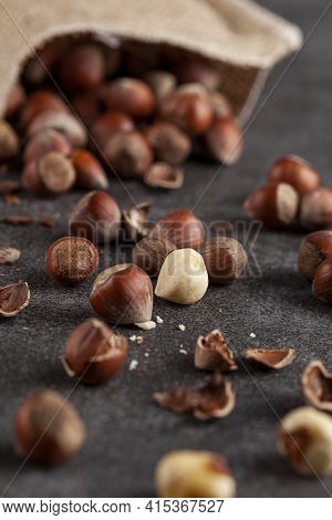 Closeup Selective Focus Image Of Hazelnuts In Shells Scattered From A Vintage Burlap Sack Onto Dark 