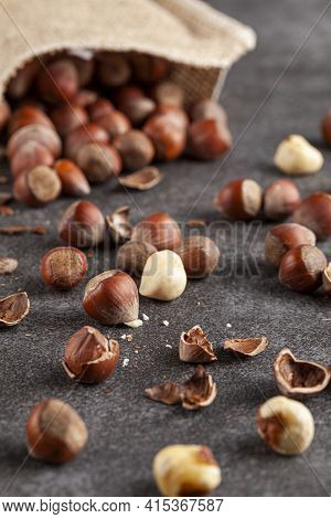 Closeup Selective Focus Image Of Hazelnuts In Shells Scattered From A Vintage Burlap Sack Onto Dark 