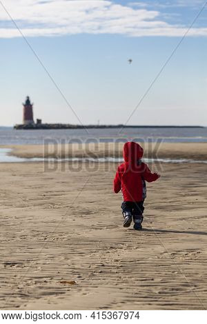 An Active Toddler Is Running Alone On The Lewes Beach Of Delaware In A Sunny But Cold Winter Day. Th
