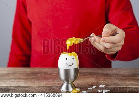 A Small Child Is Eating Soft Boiled Humpty Dumpty Egg Placed In Egg Cup On A Wooden Breakfast Table.