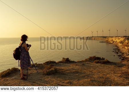 A Pregnant Woman Photographer Wearing Floral Summer Dress And A Backpack Is Taking A Landscape Photo