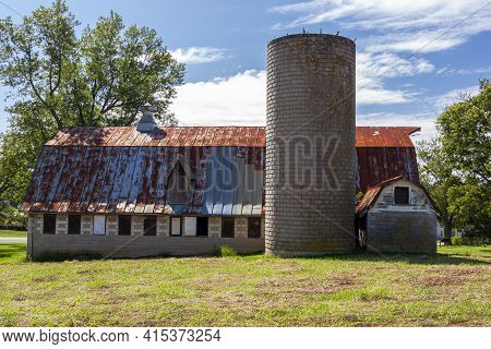 An Abandoned Old Farm House With A Tall Brick Silo And A Big Barn With Rusted Tin Ceiling. This Very