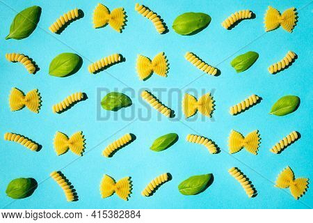 Uncooked Curly Pasta And Basil Leaf Pattern On Blue Background. Traditional Dry Raw Macaroni Pattern