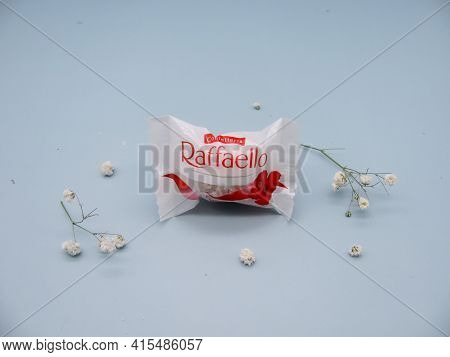One Rafaello Candy Wrapped On A Blue Background Among Flowers