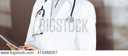Unknown Woman Doctor Iusing Tablet Computer In Her Hands, While Standing In Clinic. Medicine Concept