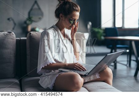 Woman Sits At Home On The Couch In A Nightgown With A Laptop