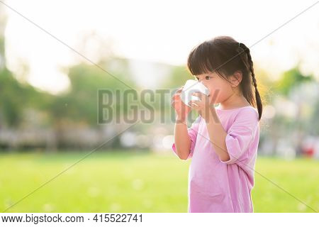 Adorable Asian Child Girl Are Drinking Fresh Water From Plastic Glasses. Green Natural Background. I