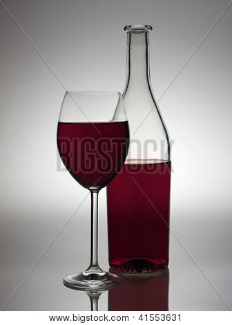 Sklo a láhev červeného vína v zadním světle.
