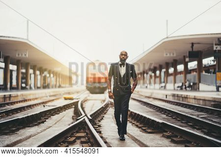 A Dapper Bearded Bald Black Guy In Glasses And An Elegant Suit With A Bow-tie Is Walking On The Trai