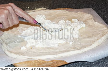 A Home Cook Is Speading Ricotta Cheese On Pizza Dough With A Spoon To Make A White Pizza.