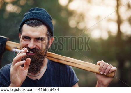 Laughing Adult Bearded Stylish Man In A Dark Sleeveless T-shirt And In A Warm Hat With A Large Musta