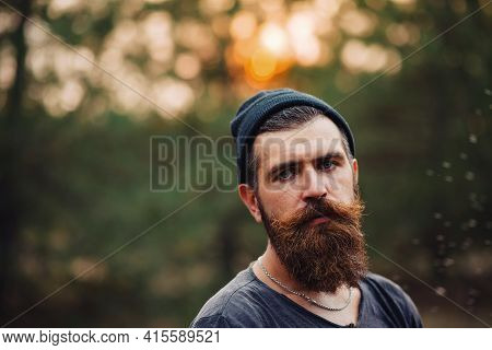 A Man With A Thick Beard And A Large Mustache In A Dark Sleeveless T-shirt And In A Warm Hat And Gra