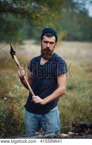 Brutal Man With A Thick Beard And A Large Mustache In A Dark Sleeveless T-shirt And A Warm Hat With