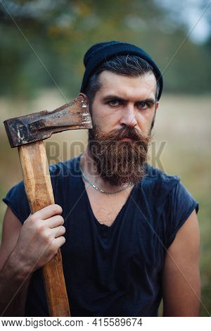 A Bearded Man With A Large Mustache In A Dark Sleeveless T-shirt And A Warm Hat With Gray Hair Holds