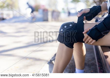 Close Up Woman Surf Skate Board Putting On Knee Protector Pads On Her Arm And Wearing Wrist Guards. 