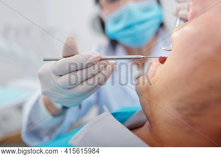 Close-up Image Of Dentis Using Small Mirror And Carver When Examining Teeth Of Male Patient