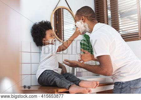 Cheerful African American Man And Little Boy Having Fun Laughing With Shaving Foam On Their Faces In