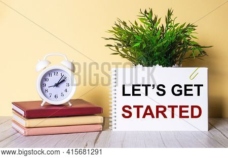Let Is Get Started Is Written In A Notebook Next To A Green Plant And A White Alarm Clock, Which Sta