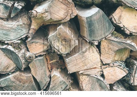 Old Firewood Or Fuelwood Stacked By A Wall. Texture Woodpile