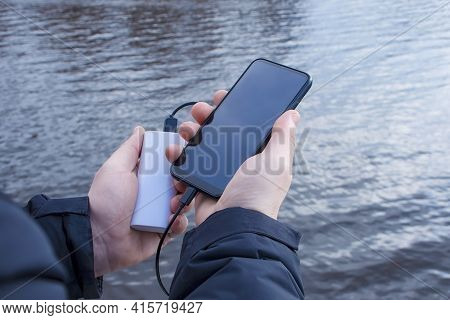 A Man Charges A Smartphone With A Power Bank. The Phone In Hand Is Being Charged With A Portable Cha