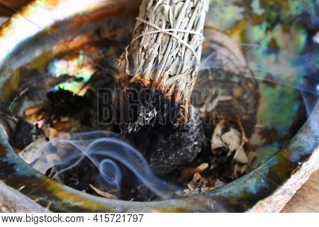 A Close Up Image Of A Burning White Sage Bundle In An Abalone Shell.