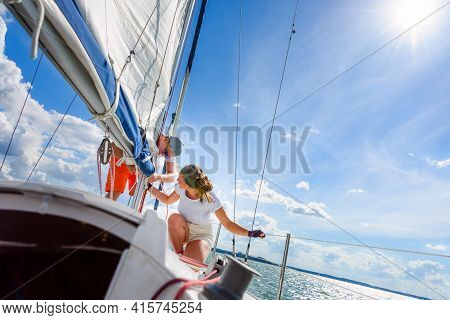 Young Woman And Man Sailing On A Yacht. Sailboat Crewmember Trimming Main Sail During Sail On Vacati
