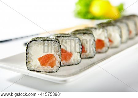Philadelphia Sushi Roll made with Smoked Salmon. Maki sushi with nori seaweed outside, salmon and cream cheese inside. White plate with wooden chopsticks on white table