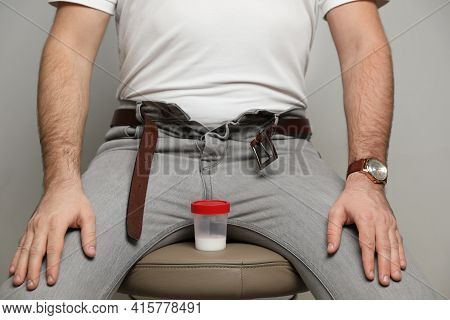 Donor With Unzipped Pants And Container Of Sperm Sitting On Stool Against Beige Background, Closeup