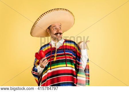 Portrait Of Man In Bright Garment And Sombrero Isolated Over Yellow Background