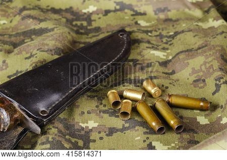 A Knife And Some Random Casings On Camouflage Cloth. Black Leather Sheath With Knife And Group Of Pi