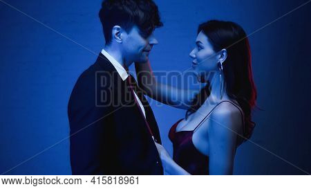 Side View Of Seductive Woman Embracing Smiling Man In Blazer On Blue.