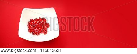 Krill Oil Capsules.banner. Red Gelatin Capsules With Krill Oil In A White Ceramic Cup On A Red Backg