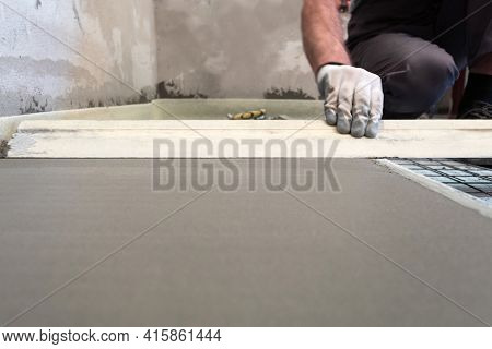 Construction Worker Performs Floor Screed Indoors. Leveling The Floor.
