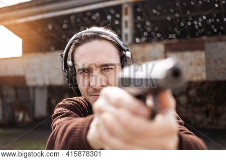 A Man Shoots A Gun, Aiming At The Target. A Man Wearing Protective Headphones. A Wall And A Roof Wit