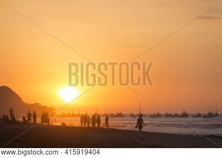 Silhouette Of People On The Beach Of Mancora During A Fantastic Orange Sunset With The Harbor In The