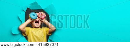 Happy cute boy is having fun played with donuts on black background wall. Bright photo of a child. Colored donuts