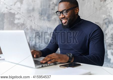 Happy Smart African-american Businessman Wearing Stylish Eyewear And Turtleneck Using The Laptop Com