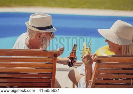 Happy Senior Couple Relaxing On A Summer Vacation, Sunbathing At Sun Beds By The Swimming Pool, Maki