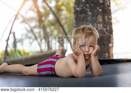 Portrait Of Cute Bored Little Caucasian Funny Sad Blond Toddler Boy Lying Inside Big Black Trampolin